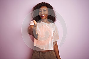 Young african american woman wearing t-shirt standing over  pink background smiling friendly offering handshake as