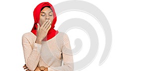 Young african american woman wearing traditional islamic hijab scarf bored yawning tired covering mouth with hand