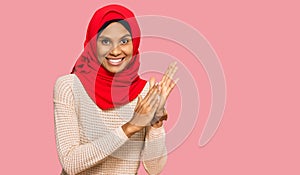 Young african american woman wearing traditional islamic hijab scarf clapping and applauding happy and joyful, smiling proud hands