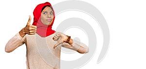 Young african american woman wearing traditional islamic hijab scarf doing thumbs up and down, disagreement and agreement