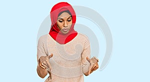 Young african american woman wearing traditional islamic hijab scarf pointing down with fingers showing advertisement, surprised