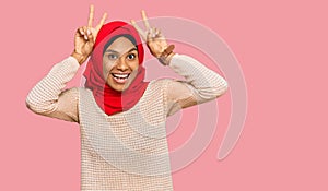 Young african american woman wearing traditional islamic hijab scarf posing funny and crazy with fingers on head as bunny ears,