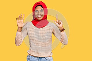 Young african american woman wearing traditional islamic hijab scarf showing and pointing up with fingers number seven while