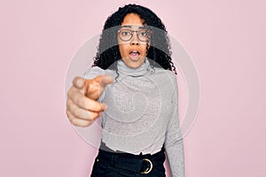 Young african american woman wearing turtleneck sweater and glasses over pink background pointing displeased and frustrated to the