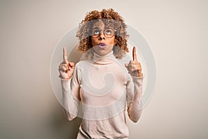 Young african american woman wearing turtleneck sweater and glasses over white background amazed and surprised looking up and