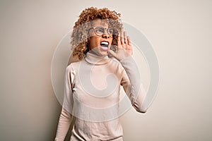 Young african american woman wearing turtleneck sweater and glasses over white background shouting and screaming loud to side with