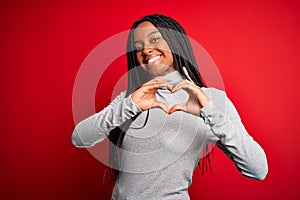 Young african american woman wearing turtleneck sweater over red isolated background smiling in love showing heart symbol and