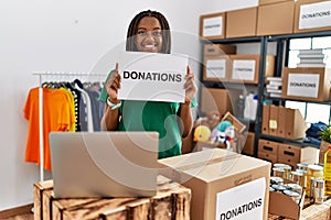 Young african american woman wearing volunteer uniform holding donations banner at charity center
