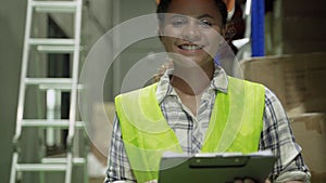 A young African American woman worker working in a warehouse, looking at the clipboard in his hand, smiling.