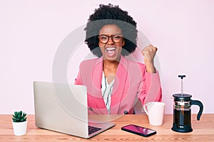 Young african american woman working at desk using computer laptop screaming proud, celebrating victory and success very excited