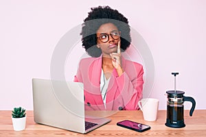 Young african american woman working at desk using computer laptop serious face thinking about question with hand on chin,
