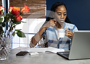 Young, African American woman working from home on her laptop in the kitchen