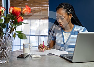 Young, African American woman working from home on her laptop in the kitchen