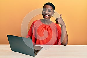 Young african american woman working at the office with laptop smiling happy and positive, thumb up doing excellent and approval