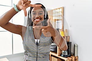 Young african american woman working at the office wearing operator headset smiling making frame with hands and fingers with happy