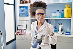 Young african american woman working at scientist laboratory doing make up smiling happy and positive, thumb up doing excellent