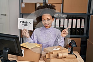 Young african american woman working at small business ecommerce holding thank you banner smiling happy pointing with hand and