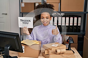 Young african american woman working at small business ecommerce holding thank you banner smiling happy and positive, thumb up