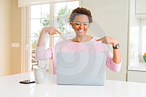 Young african american woman working using computer laptop looking confident with smile on face, pointing oneself with fingers