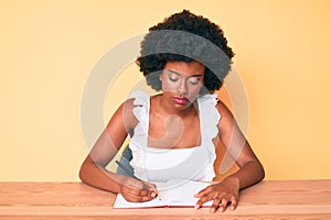 Young african american woman writing book thinking attitude and sober expression looking self confident