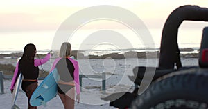 Young african american woman and young caucasian woman going surfing at dawn, with copy space