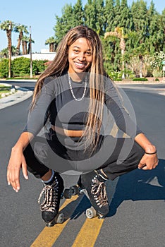 Young African-American women with roller skates squats on the street