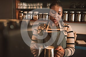 Young African barista making a cappuccino behind her cafe counter