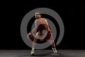 Young african basketball player training on black studio background.