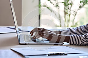 Young African black female hands typing on laptop computer keyboard.