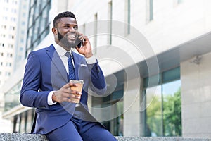 Young african businessman speaking on the phone with a cup of coffee while sitting outside