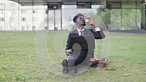 Young African bussiness man in formalwear working on laptop computer while sitting outdoors