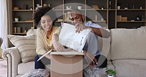 Young African couple sit on sofa unpack parcel box