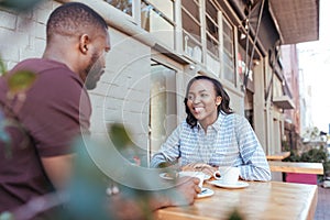 Young African couple talking together at a sidewalk cafe table