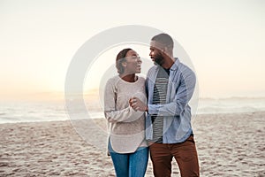 Young African couple walking on a beach at sunset laughing