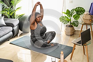 Young African curvy woman doing pilates online fitness class with laptop at home