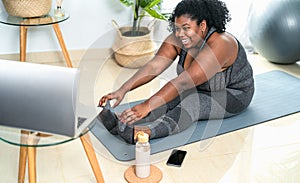 Young African curvy woman doing pilates online fitness class with laptop at home