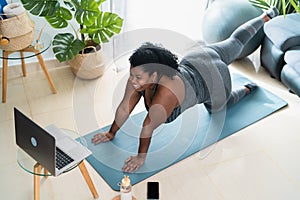Young African curvy woman doing pilates virtual fitness class with laptop at home photo