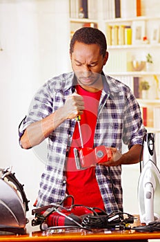 Young African Ecuadorian male Technician pucker his face having problems while he is fixing a red sander with a