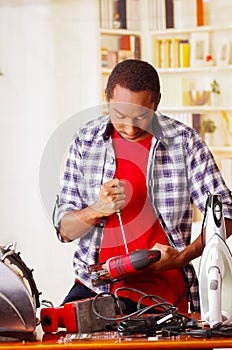 Young African Ecuadorian male Technician pucker his face having problems while he is fixing a red wood sander with a