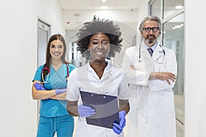 Young African female doctor smiling while standing in a hospital corridor with a diverse group of staff in the background