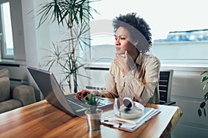 Young African female entrepreneur sitting at a desk in her home office working online with a laptop