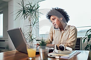 Young African female entrepreneur sitting at a desk in her home office working online with a laptop