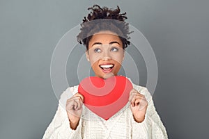 Young african woman isolated on grey wall studio winter concept holding heart close-up thinking