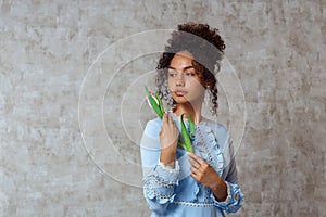 Young African girl in a blue dress with a Tulip on a gray background. The concept of women`s day and spring