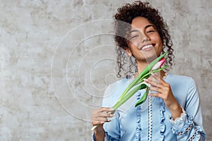 Young African girl in a blue dress with a Tulip on a gray background. The concept of women`s day and spring