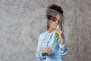 Young African girl in a blue dress with a Tulip on a gray background. The concept of women`s day and spring