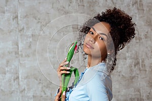 Young African girl in a blue dress with a Tulip on a gray background. The concept of women`s day and spring