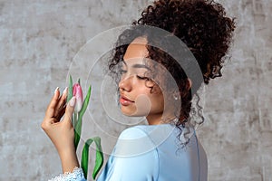 Young African girl in a blue dress with a Tulip on a gray background. The concept of women`s day and spring