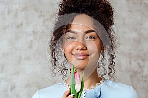 Young African girl in a blue dress with a Tulip on a gray background. The concept of women`s day and spring