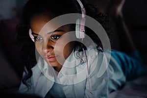 Young african girl in headphones liying in front of laptop